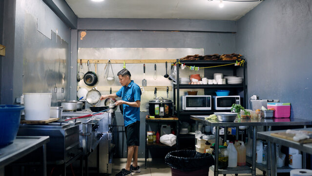 Busy Latino chef stirring food in a pan, preparing a meal inside a small, somewhat cluttered commercial restaurant kitchen