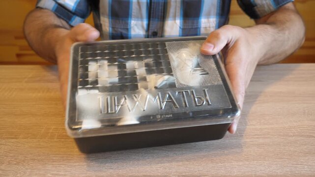A man shakes a plastic package with chess pieces, creating a distinctive plastic rattling sound. The video contains clean original audio.