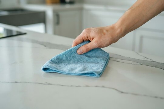 A hand wipes a marble countertop with a blue cloth. Hygiene concept.