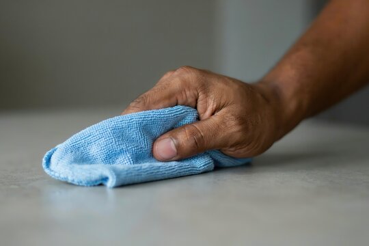 A hand wipes a grey kitchen surface with a blue cloth. Hygiene concept.