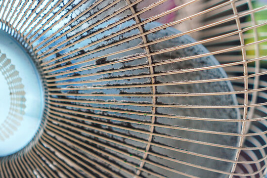 Close-up of dusty electric fan grille showing accumulated dirt and debris, highlighting maintenance needs for household appliances. Ideal for home improvement, cleaning, or appliance care themes.