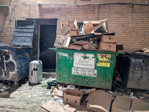 MONTREAL, CANADA, 22 December 2025 : Overflowing dumpster, cardboard boxes, suitcase, brick wall, alleyway