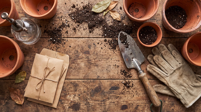 Gardening tools, soil, and terra cotta pots arranged on a rustic wooden table, ready for planting new seeds