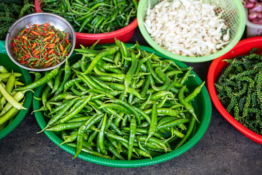 Basins full of fresh hot chili peppers, garlic and green peppercorns on sale at street food market, wholesale of exotic spices and vegetables at bazaar, containers filled with various food ingredients