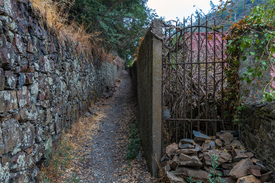 A narrow dirt alley framed by rustic schist stone walls