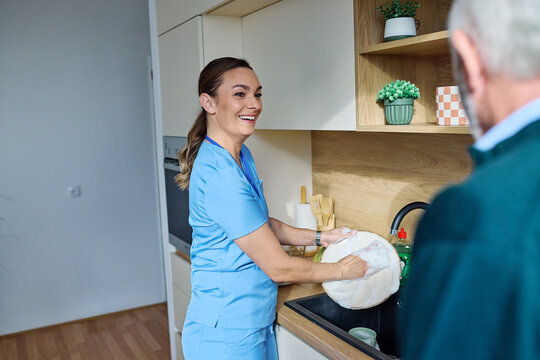 Portrait of a doctor or nurse caregiver supporting senior man, A caregiver cleans dishes at a kitchen sink with an elderly person observing.  in kitchen at home or nursing home