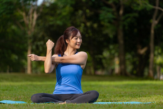 Asian woman relaxingly practicing shoulder stretch yoga for cool down after exercise inside the public park