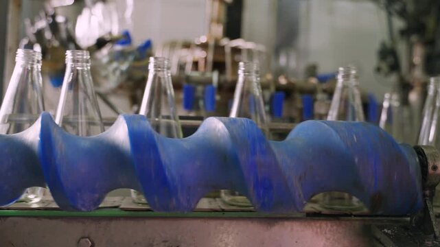 Empty glass beverage bottles on an automatic conveyor belt in a manufacturing plant. Technology for manufacturing bottles and filling fruit juice. Drinking water bottle on factory production conveyor.