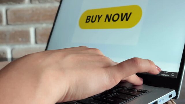 Person using laptop touchpad to click yellow buy now button on screen, engaging in online shopping and e commerce transactions for a quick purchase from a retail website