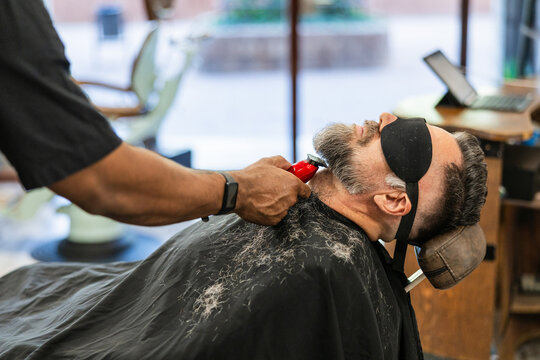 Barber trimming client's beard with electric clipper