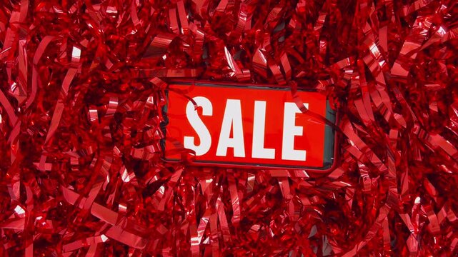 Smartphone with red sale screen on shiny tinsel, advertising a discount shopping promotion. Great for black friday, cyber monday, or holiday season marketing