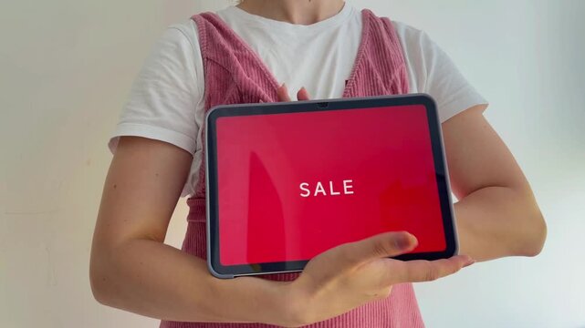 Woman opening a tablet computer revealing a big red sale announcement on the screen, isolated on a white background, representing online shopping and black friday deals