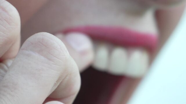 Dental hygiene examination shows a woman checking her white teeth using a finger indoors. Macro extreme close up shot captures clear facial detail.