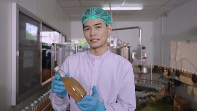 Professional Asian inspector in uniform of food and drink factory holding a juice beverage bottle promoting and advertising healthy nutritional benefits in production line at a manufacturing industry.