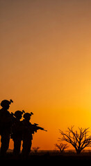 Obraz premium Silhouettes of soldiers with rifles stand in a desert landscape at sunset, symbolizing strength, vigilance, and resilience against a warm, vibrant sky