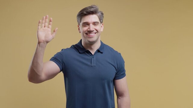 Friendly adult man smiling and waving hello to camera with an open hand gesture. Handsome male greeting, welcoming visitors, saying hi or goodbye. Perfect for business communication, customer service
