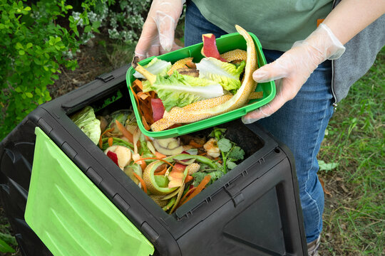 Woman throwing kitchen scraps into a compost bin in a garden