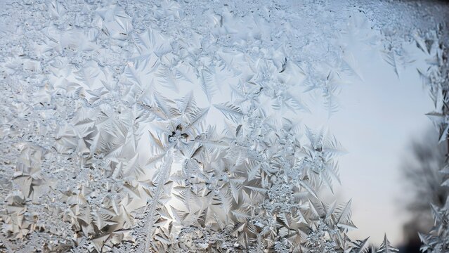 Detailed close up of intricate ice crystals forming a frozen pattern on a glass window surface during cold winter