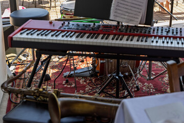 Fototapeta premium A red stage keyboard with sheet music leads a layered small-band setup, with a saxophone bell in front and an acoustic drum kit behind.