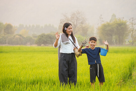Happy Asian boy showing muddy hands to smiling mother in green rice field, playful child and mom bonding outdoor, fun rural childhood experience, traditional agricultural lifestyle and family love
