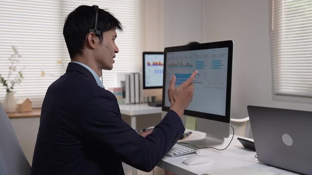 Asian male call center agent talking with headset in front of computer monitor in office