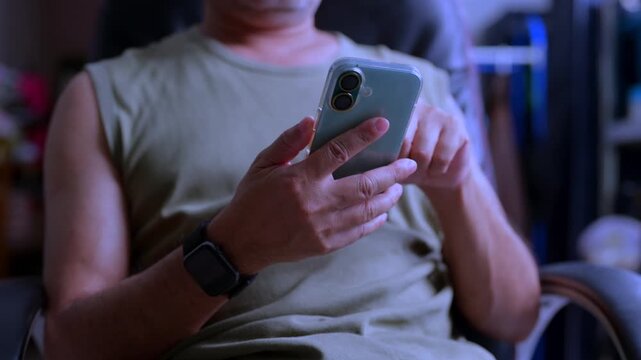Adult male user holding smartphone typing message indoor setting wearing smartwatch demonstrating mobile technology connectivity digital communication daily routine lifestyle.
