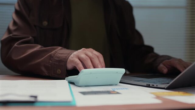 Adult person sitting office desk calculating financial expenses reviewing tax reports typing laptop keyboard analyzing budget data planning economy strategy commercial accounting corporate paperwork.