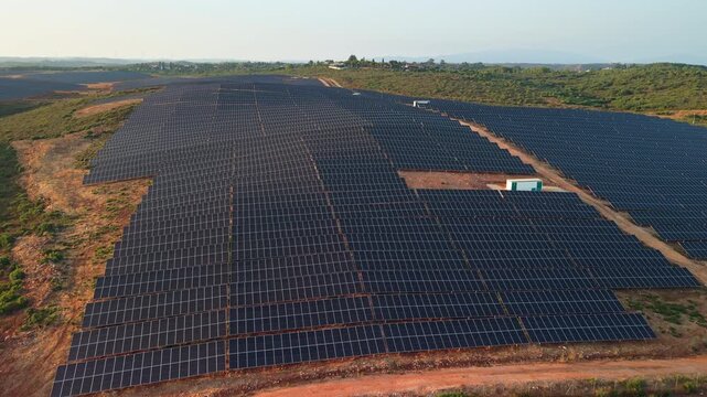 Aerial panoramic view of a large photovoltaic power station with thousands of solar panels covering rolling countryside