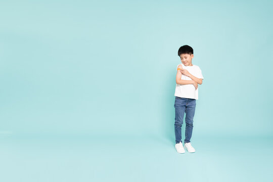 A brave Asian boy looking at a bandage on his arm after getting vaccinated in studio, showing child immunization, healthcare, medical protection, and health safety with copy space