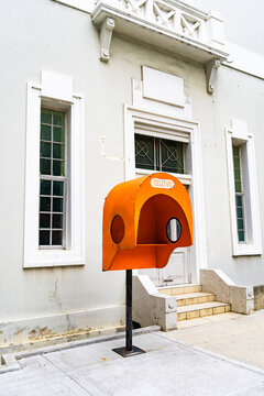 Bright orange outdoor security call box against a white building