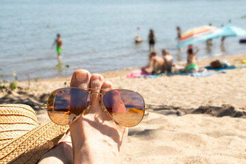 Women's legs on a sandy beach next to a straw hat and sunglasses. The theme is summer vacation, holiday, resort © Виктория Котлярчук