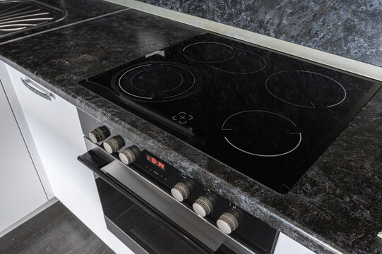 black glass-ceramic electric hob with four burners, integrated into a dark marble-effect countertop. below is a built-in oven with rotary knobs and a digital display.