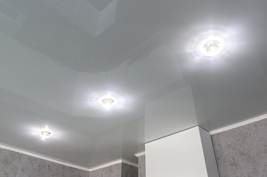 glossy white stretch ceiling with recessed spotlights, gray textured walls, and white crown molding accenting the ceiling-wall junction