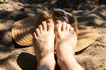 Women's legs on a sandy beach next to a straw hat and sunglasses. The theme is summer vacation, holiday, resort © Виктория Котлярчук