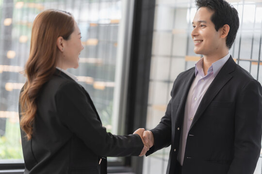 Close up of smiling Asian businessman and businesswoman shaking hands in corporate office.