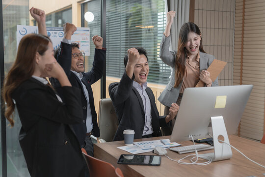 Group of cheerful Asian business people celebrating success with arms raised in office.