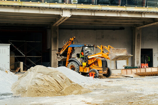 Yellow backhoe loader and sand pile on a construction ground