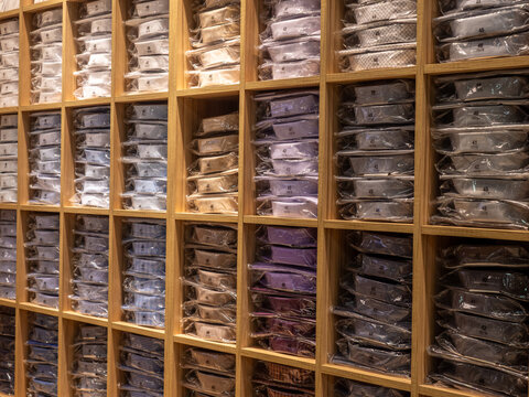 Rows of neatly folded, plastic-wrapped men's dress shirts sorted by size and color on wooden shelving compartments in a retail store.