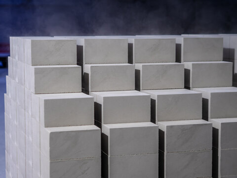 Smooth light gray concrete blocks stand neatly stacked in precise rows surrounded by light steam inside an industrial production facility.