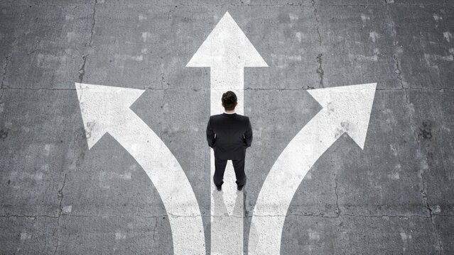 Businessman standing at crossroads with arrows on pavement choosing direction and career path