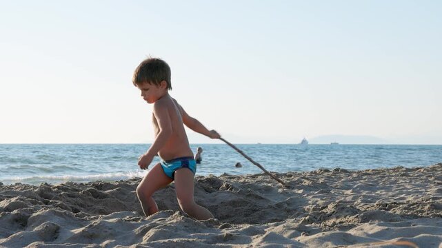 Young Boy Playing with Stick on Sunny Sandy Beach by the Ocean