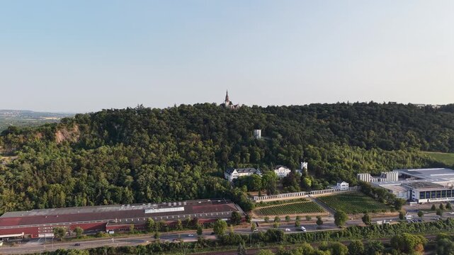 Drone aerial view of Klopp Castle hill in Bingen am Rhein, Germany, featuring the forested hillside crowned by Klopp Castle, vineyards, historic architecture and the Rhine riverside below. Scenic summ