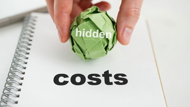 Hand holding green crumpled paper with hidden text over notebook with costs word