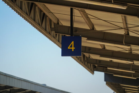 Blue numbered platform sign hanging from metal roof structure at train station under clear sky, industrial architecture with exposed beams and lighting fixtures for travel or transportation concepts.