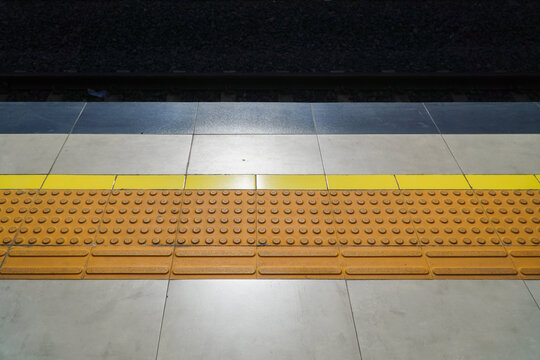 Close-up of a train station platform with tactile paving and yellow safety line, showing urban transit infrastructure for accessibility and safety, elegantly showcasing public.