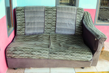 Obraz premium Worn vintage sofa with quilted green pattern sits against colorful wall near window, showing signs of age and use for home decor or furniture restoration projects, elegantly showcasing old.