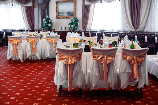 Elegant wedding reception banquet set in classic ballroom with white-draped chairs tied with gold bows, decorated tables, glassware, creating formal, festive atmosphere for celebration and dining