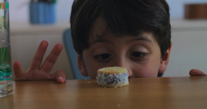 Young boy watches a small coconut dessert on home dining table, studying the sweet treat with curiosity, anticipation, temptation and playful childhood self-control