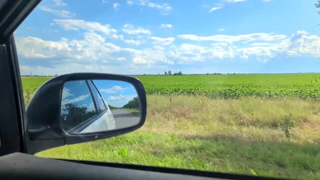 Car Side Mirror Reflection Showing Road and Blue Sky During Driving on Country Road. Driving Motion View Through Car Window with Side Rearview Mirror Reflection