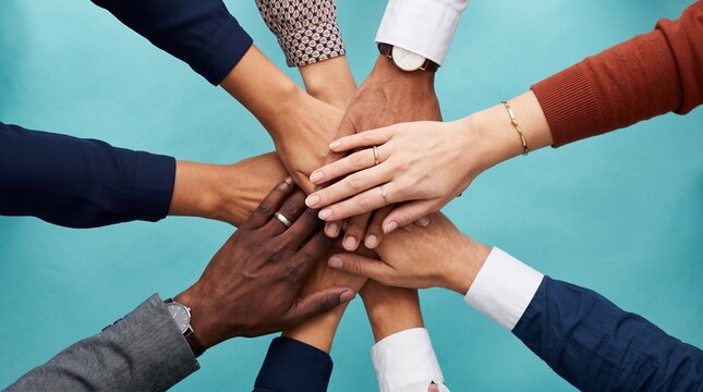 A diverse group of hands stacked together in a symbol of unity and teamwork, against a teal backdrop, showcasing cooperation and connection.